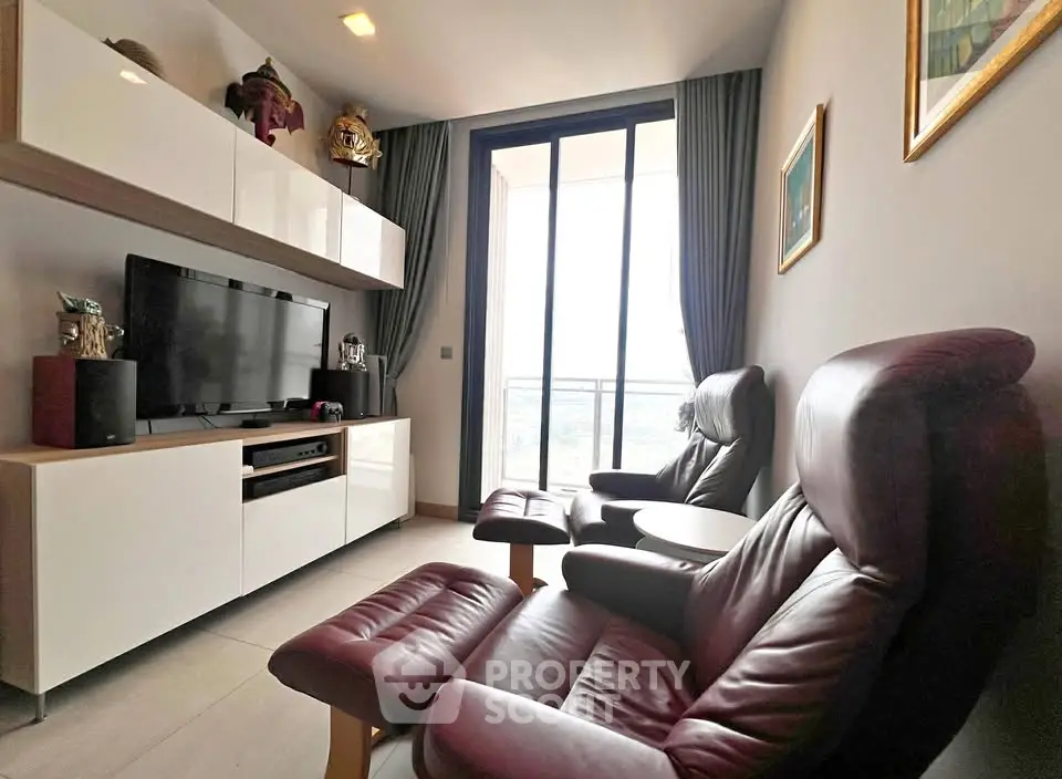 Modern living room with leather chairs and entertainment center, featuring large windows and balcony access.