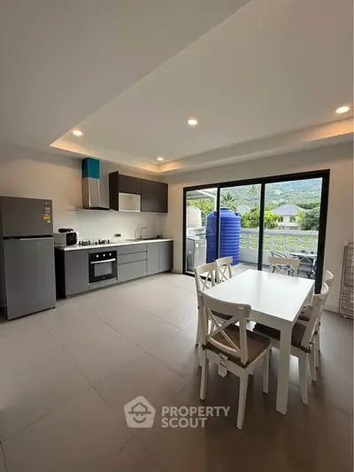 Modern kitchen with dining area and mountain view from balcony, featuring sleek appliances and open layout.