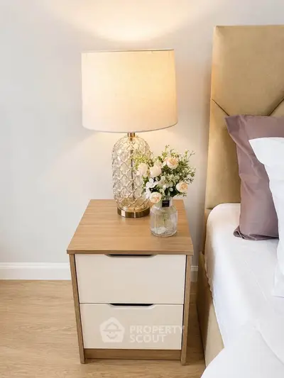 Elegant bedroom nightstand with lamp and floral decor beside a cozy bed, showcasing modern interior design.