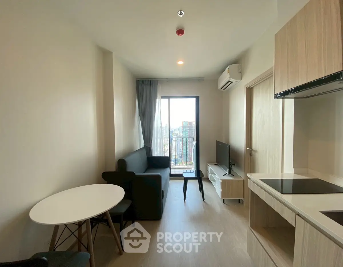 Modern living room with balcony view, sleek furniture, and open kitchen layout.