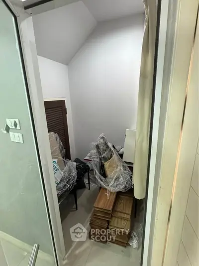 Compact storage room with stacked wooden planks and covered furniture, ideal for organizing household items.