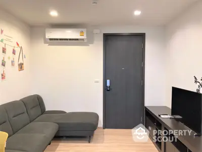 Modern living room with sleek furniture and wooden flooring, featuring a comfortable grey sectional sofa and a flat-screen TV, perfect for urban living.