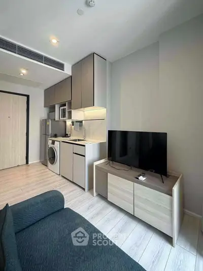 Modern compact living room with integrated kitchen and washing machine, featuring sleek cabinetry and a flat-screen TV.