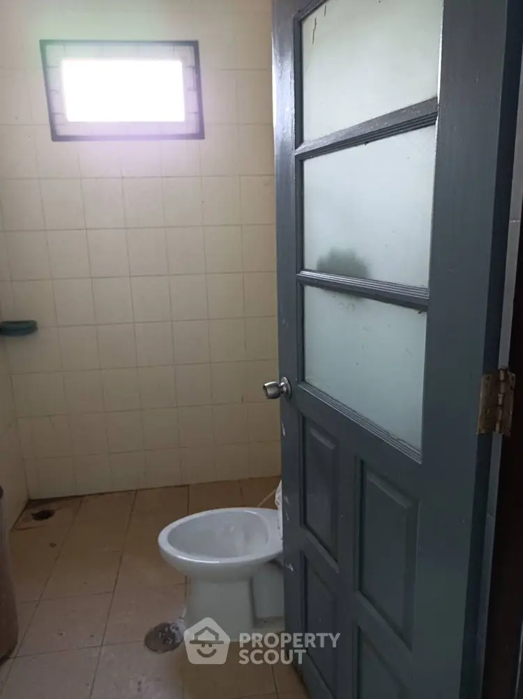Simple bathroom with frosted glass door and small window, ideal for compact spaces.