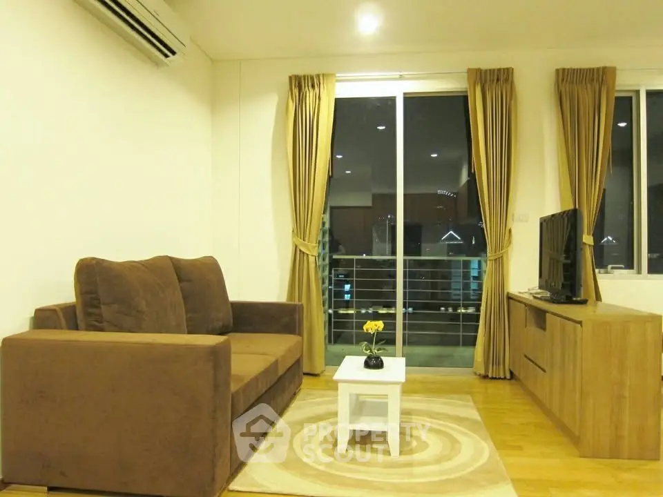 Cozy living room with brown sofa, TV, and balcony view in modern apartment.