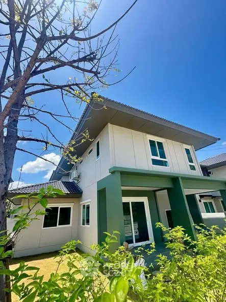 Modern two-story house with green accents and lush garden under a clear blue sky.