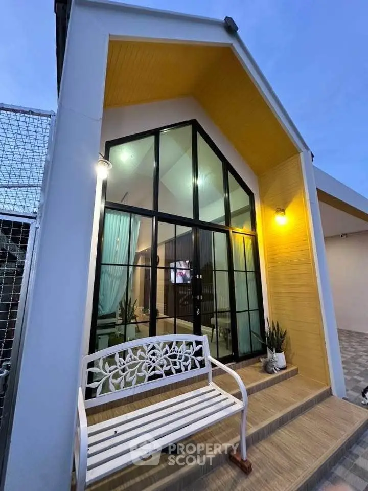 Charming modern house exterior with large glass windows and inviting entrance bench.