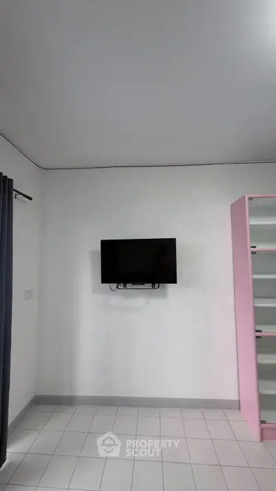 Minimalist room with wall-mounted TV and pink shelving unit, ideal for modern living.