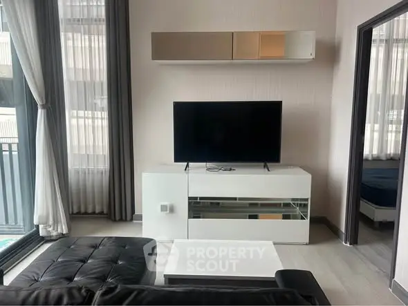 Modern living room with sleek black sofa and large TV, adjacent to a balcony.
