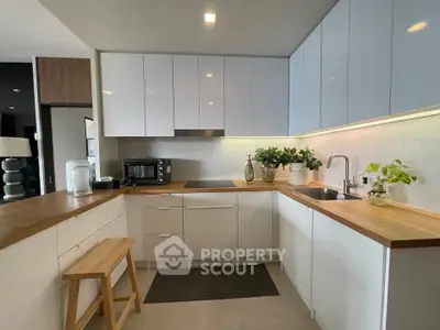 Modern kitchen with sleek white cabinets and wooden countertops, featuring a built-in oven and stylish decor.