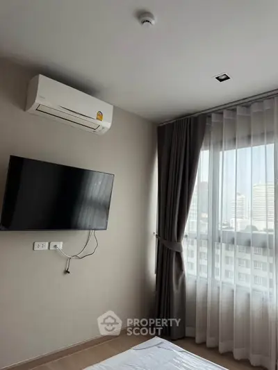 Modern bedroom with wall-mounted TV and air conditioning, featuring large window with city view.
