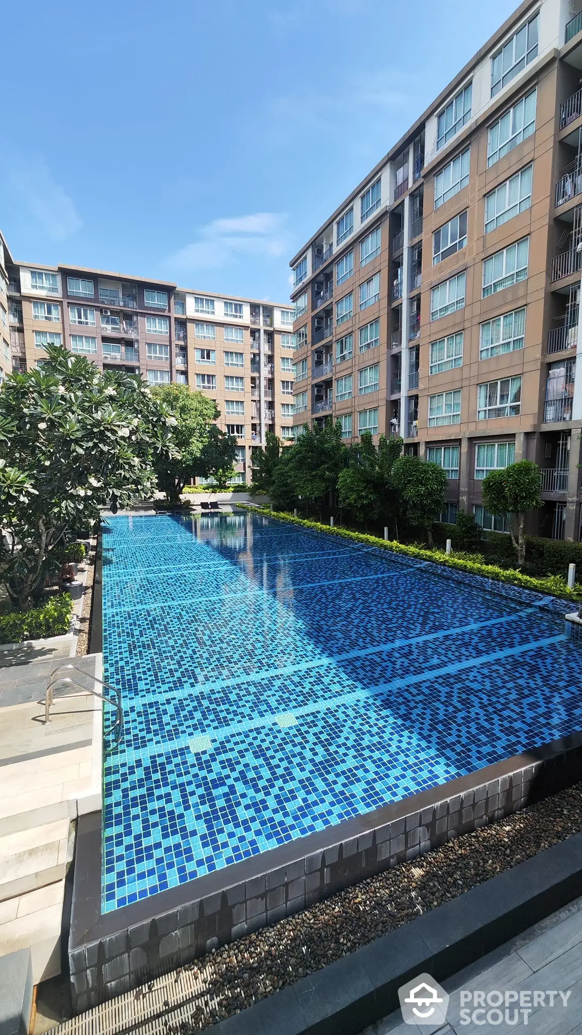 Luxurious residential complex with a sparkling blue communal pool surrounded by lush greenery and modern apartment buildings, offering a serene urban oasis.