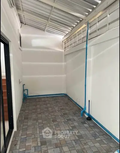 Spacious tiled area with covered roof and plumbing, ideal for utility or storage use.
