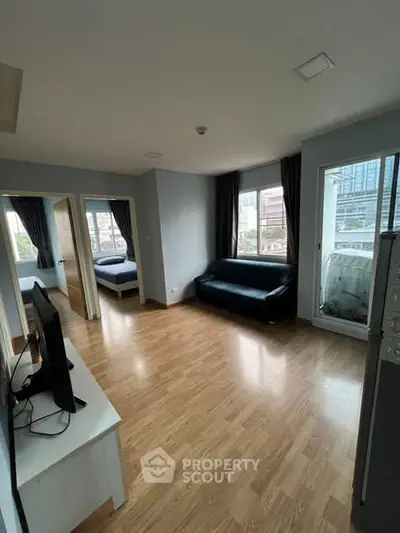 Spacious living room with wooden flooring and city view, featuring a cozy sofa and modern TV setup.