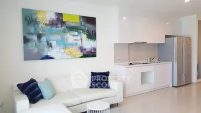 Modern living room with sleek kitchen and abstract art, featuring a cozy white sofa and stainless steel fridge.