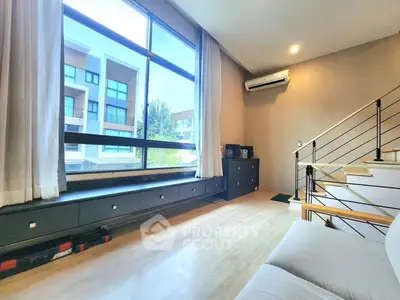 Modern living room with large window and staircase, featuring air conditioning and sleek design.