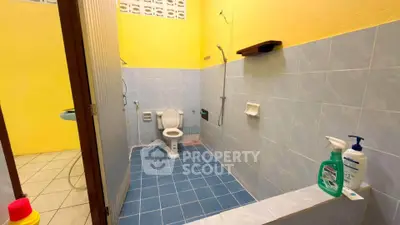 Spacious bathroom with vibrant yellow walls and blue tiles, featuring modern fixtures and cleaning supplies.