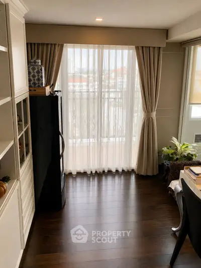 Charming living space with elegant curtains and balcony access, featuring hardwood floors and stylish decor.
