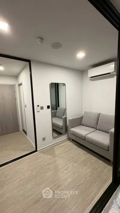 Modern living room with sleek design and cozy gray sofa, featuring a large mirror and air conditioning.