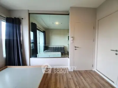 Modern apartment interior with wooden flooring and large mirror reflecting natural light.