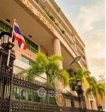 Elegant building exterior with lush palm trees and national flags, showcasing modern architecture and secure entrance.