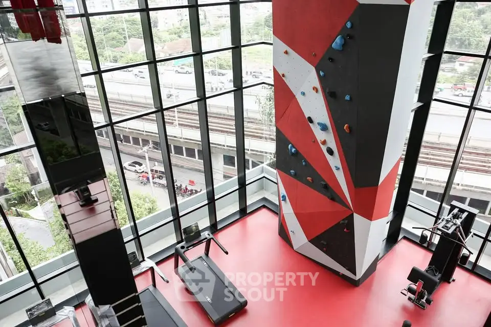 Modern gym with climbing wall and treadmills in a high-rise building with city view.