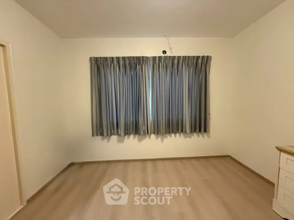 Spacious empty room with wooden flooring and large window with curtains.