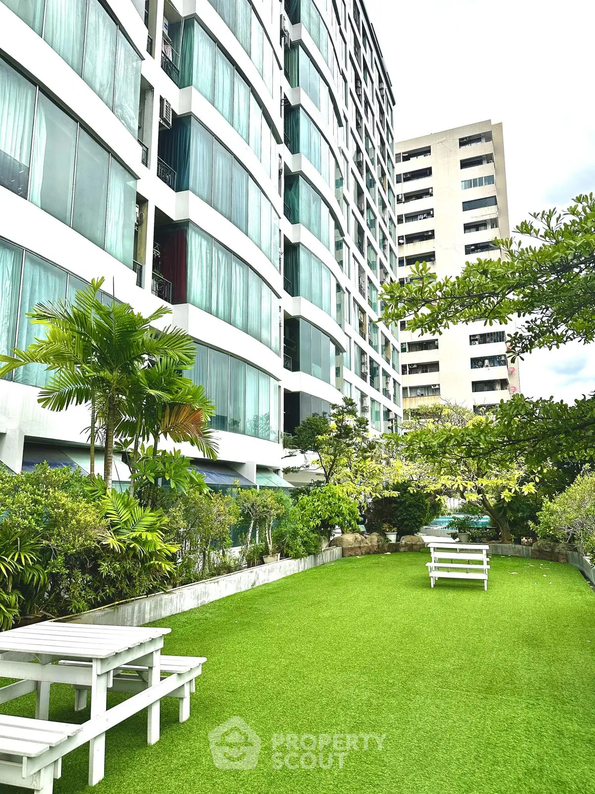Modern apartment building with lush garden and seating area, perfect for relaxation.