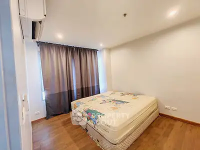 Spacious bedroom with wooden flooring and large window, featuring a comfortable bed and modern lighting.