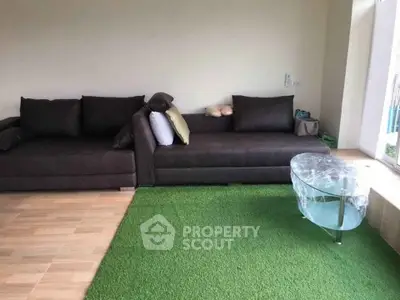 Spacious living room with modern dark sofas and unique glass coffee table on green rug.
