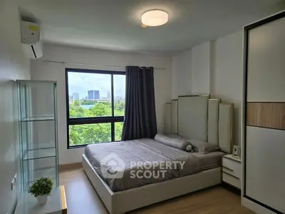 Modern bedroom with large window and city view, featuring sleek furniture and natural light.