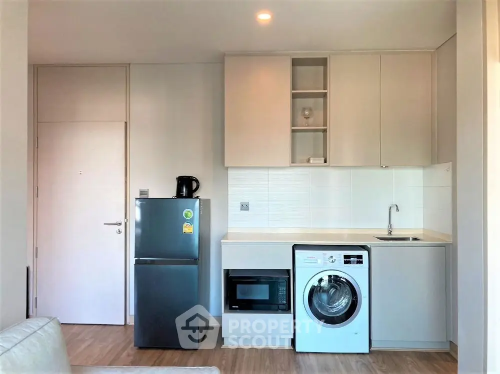 Modern kitchen with sleek appliances and compact design, featuring washing machine and fridge.