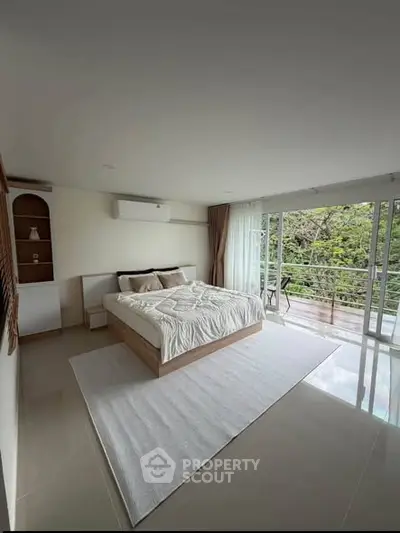 Spacious bedroom with large windows and balcony access, offering serene views and modern decor.
