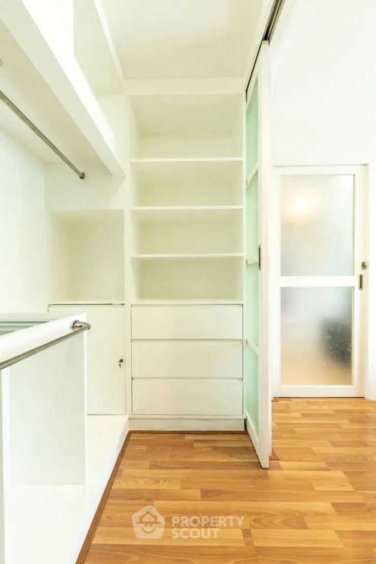 Spacious walk-in closet with wooden flooring and sliding doors in modern apartment.
