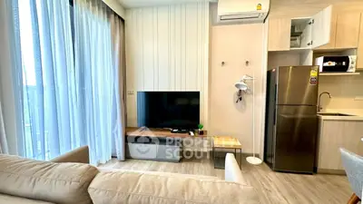 Modern living room with TV, sofa, and kitchen appliances in open layout.