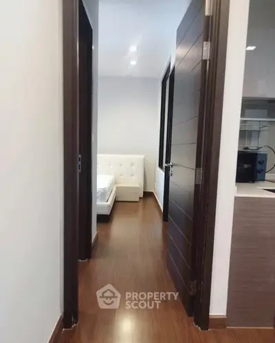 Modern apartment hallway leading to a cozy bedroom with wooden flooring.