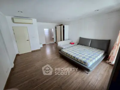 Spacious bedroom with modern furnishings and wooden flooring in a well-lit apartment.