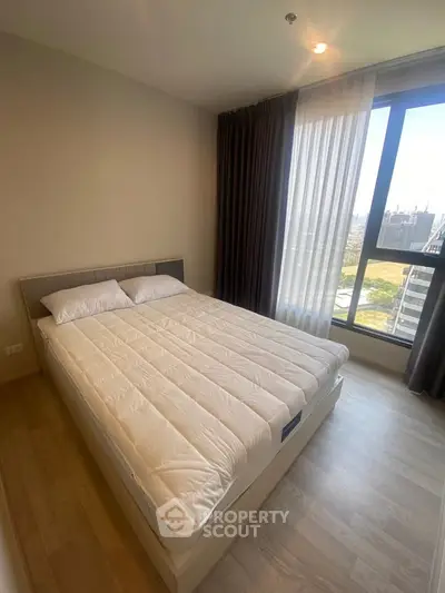Modern bedroom with large window and city view, featuring a comfortable bed and stylish curtains.