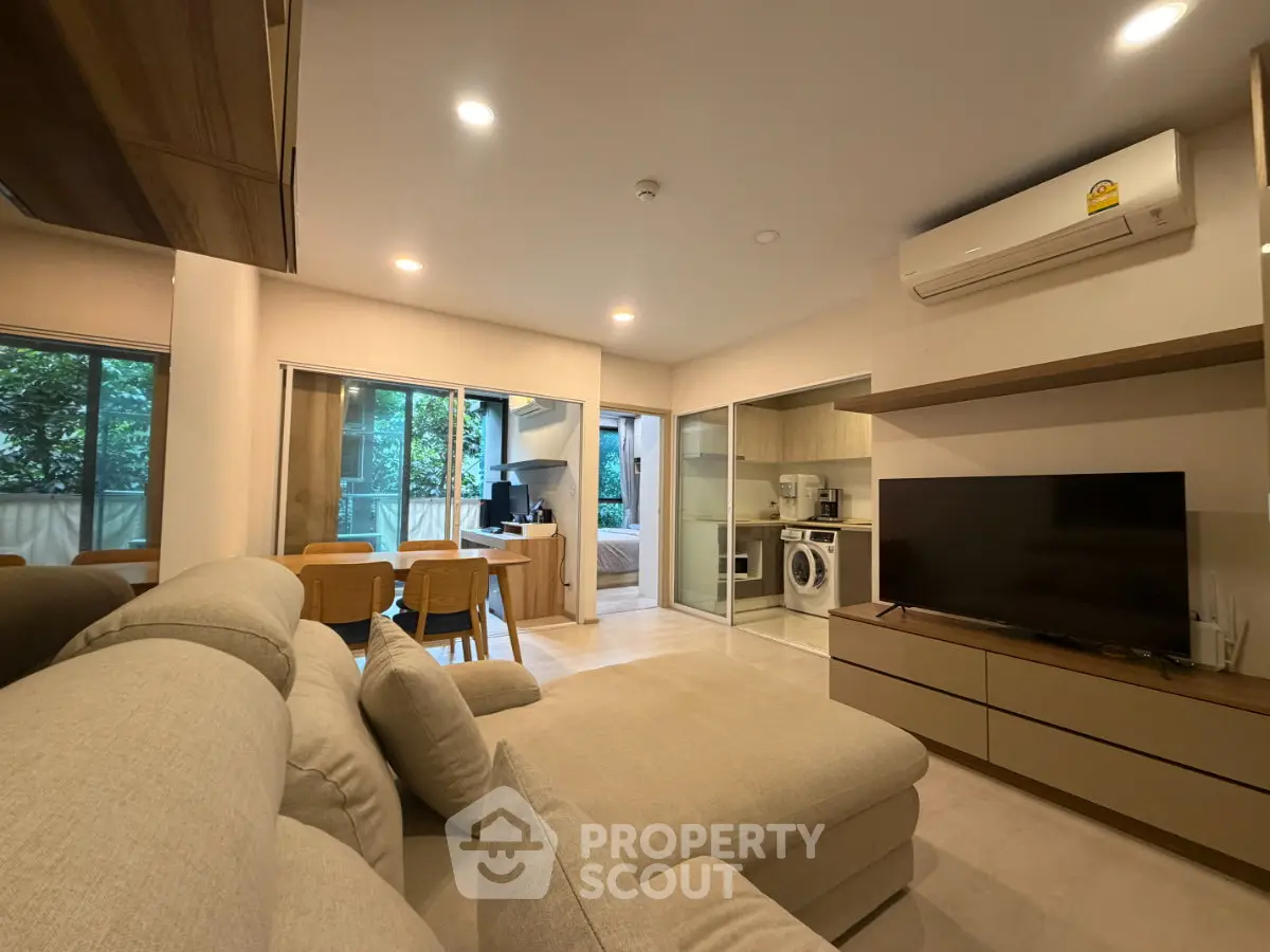 Modern open-plan living room with cozy sofa, dining area, and view into bedroom and kitchen.