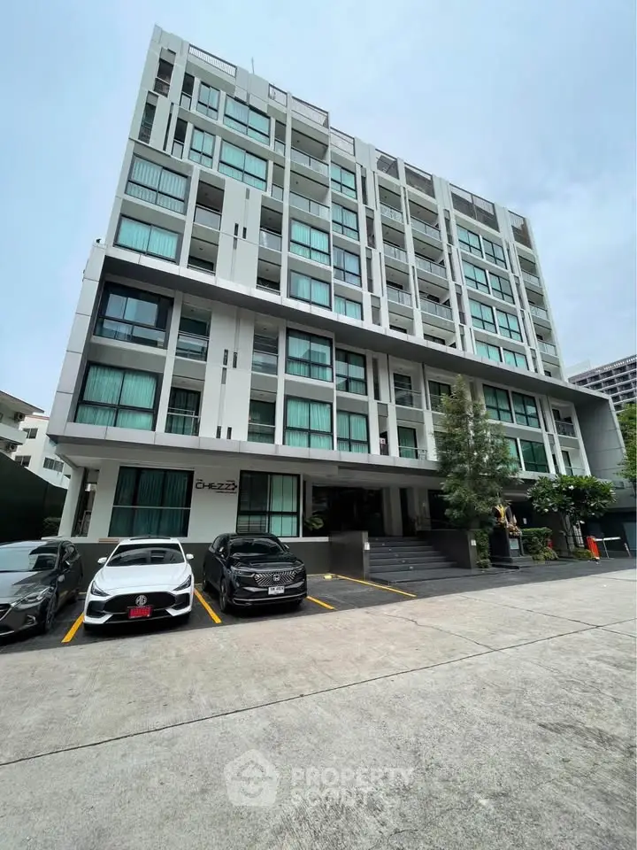 Modern multi-story apartment building with parking area and sleek architectural design.