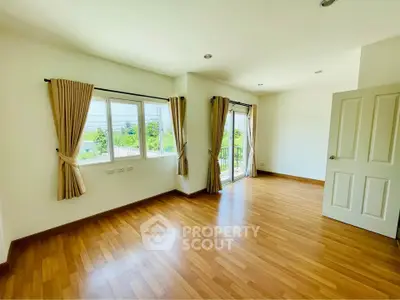 Spacious empty room with wooden flooring and large windows offering natural light.