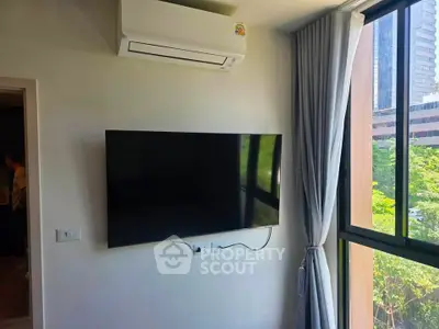 Modern living room with wall-mounted TV and large window offering city views.