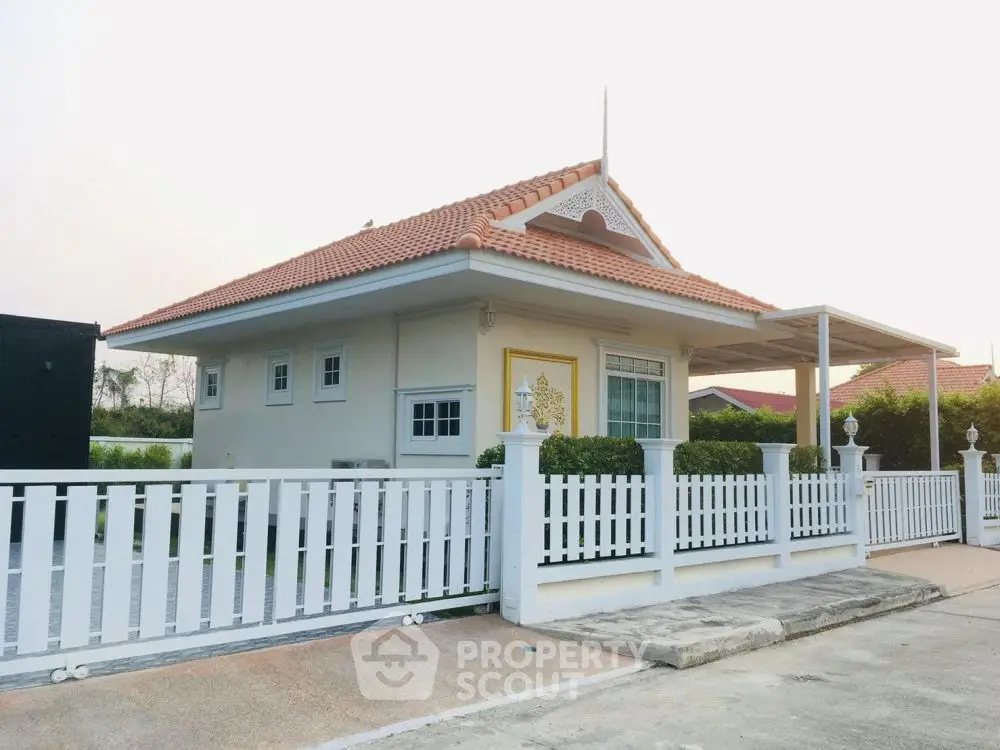 Charming single-story house with red-tiled roof and white picket fence in serene neighborhood.