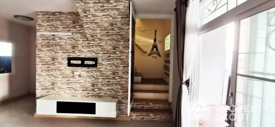 Spacious living area with modern stone accent wall and fireplace, leading to an inviting staircase and ample natural light.