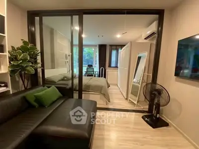Modern studio apartment with glass partition, sleek black sofa, and cozy bedroom area.