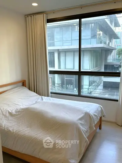 Cozy bedroom with large window offering urban view in modern apartment