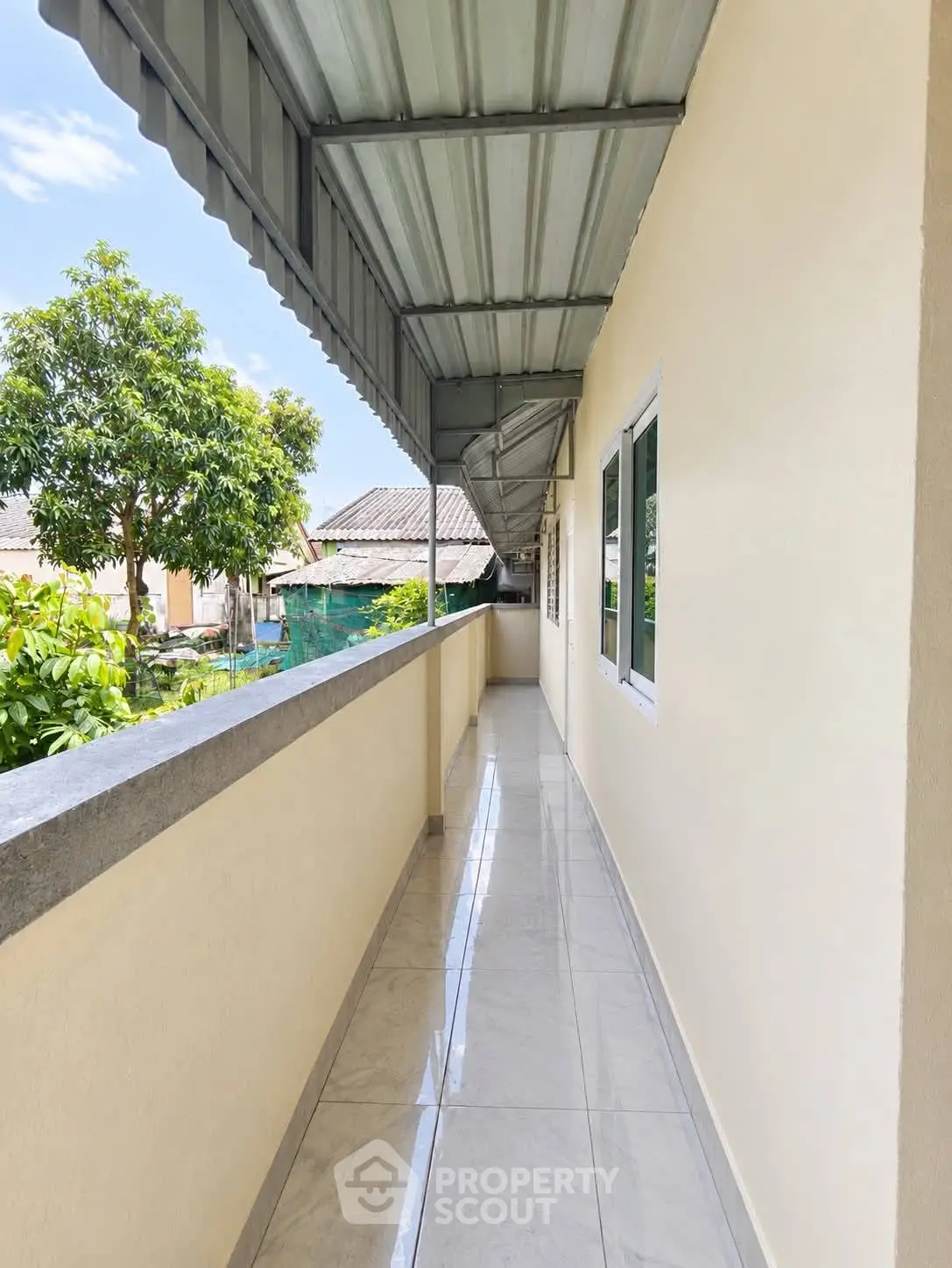 Spacious outdoor corridor with tiled flooring and metal roofing, offering a serene view of lush greenery.