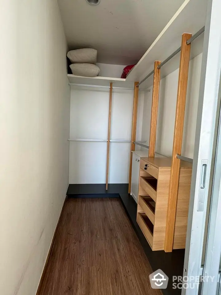 Spacious walk-in closet with wooden shelves and hanging rods, perfect for organized storage.