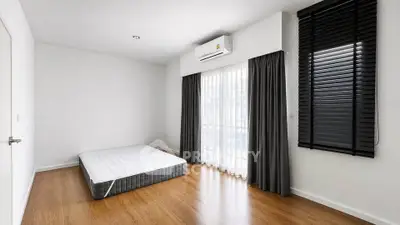 Spacious minimalist bedroom with wooden flooring and large window for natural light.