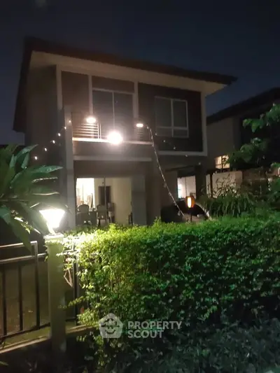 Charming two-story house with lush garden and ambient night lighting, perfect for serene living.